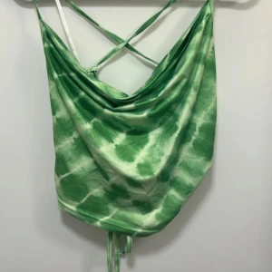 Grön tie-dye croppad linnetopp med snörning - Säljer en grön och vit tie-dye croppad linnetopp med tunna axelband som korsas i ryggen och snygg snörningsdetalj baktill. Toppen har en draperad halsringning och är perfekt för sommaren.