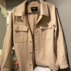 Beige overshirt jacka från Bik Bok - Säljer en beige overshirt jacka från Bik Bok i ullblandning. Jackan har en krage och silvriga fina tryckknappar framtill och två stora bröstfickor som man kan stänga. Enkel att styla till olika outfits💘 har aldrig använt !❤️