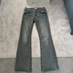 Grå bootcut jeans från Gina Tricot - Säljer ett par grå jeans från Gina Tricot i bootcut-modell. Jeansen har klassisk femficksdesign, låg midja och raka ben med lätt utsvängning. Perfekta för dig som gillar en avslappnad men ändå trendig look.