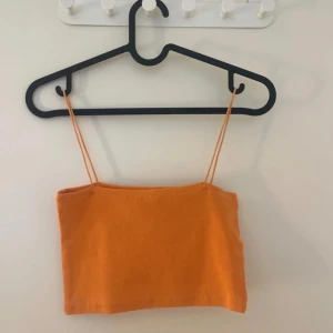 Orange ribbad croppad linnetopp från Zara - Säljer en orange ribbad croppad linnetopp från Zara med tunna axelband. Perfekt för varma dagar och enkel att matcha med jeans eller kjol. Supersnygg och trendig färg!