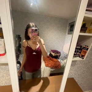 Vinröd croppad linnetopp från BikBok - Säljer en vinröd croppad linnetopp från BikBok med smala axelband och en liten cut-out detalj framtill. Toppen har en figurnära passform och är perfekt för att lyfta vilken outfit som helst.