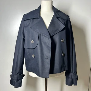 Kort trenchcoat  - Kort trenchcoat från h&m. Köptes förra året för runt 500kr. Använd ett fåtal gånger. Storlek xs men passar även storlek s. Köp sker via köp nu, jag postar inom 24h. Kvar tills markerad såld 