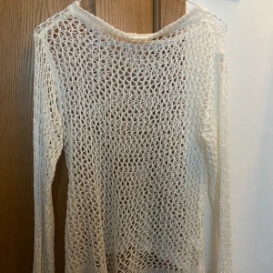 Vit stickad meshtröja - Säljer en vit stickad meshtröja med lång ärm och lös passform. Perfekt att ha över ett linne eller bikini. Tröjan har ett grovmaskigt mönster och är superlätt och luftig.