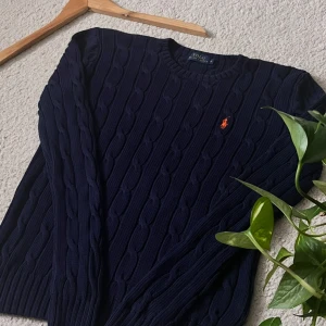 Ralph Lauren Cable Knit Tröja  - Stilren och klassisk kabelstickad tröja från Polo Ralph Lauren i marinblå färg. 	•	Storlek: Medium (M) 	•	Passform: Normal 	•	Ikoniska röda Polo-loggan broderad på bröstet 	•	Mjukt bomullsmaterial – perfekt för både vardag och lite finare tillfällen 	•	I mycket fint skick, sparsamt använd 	•	Originalprodukt  En tidlös tröja som aldrig går ur stil – perfekt att matcha med jeans, chinos eller över en skjorta.  Skick: 9/10 Nypris: ca 1 500 kr 