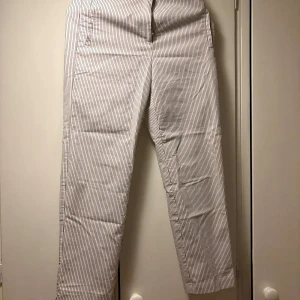 Randiga kostymbyxor från M&S - Snygga vita kostymbyxor med tunna mörkblå ränder från M&S. Klassisk rak passform och normal midja. Perfekta för stilren look och passar till många olika outfits.