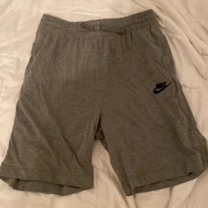 Grå shorts från Nike - Gråa shorts från Nike med elastisk midja och diskret Nike-logga på vänster ben. Tillverkade i mjukt material som passar perfekt för avslappnade dagar eller träning. Klassisk och enkel design. Pris ej spikat