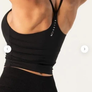 Svart croppad linnetopp från Relode - Säljer en svart croppad linnetopp från Relode med smala axelband och tight passform. Perfekt för träning eller som ett snyggt basplagg. Toppen har en stilren design med logga på ryggen.