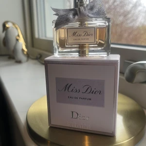 Miss Dior Eau de Parfum 30ml - Miss Dior Eau de Parfum från Dior i en elegant glasflaska med en söt grå rosett runt halsen. Parfymen kommer i en stilren vit och grå kartong med silverdetaljer. Flaskan rymmer 30 ml. Nypris 945 kr