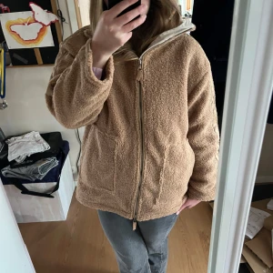 Brun teddyjacka med dragkedja - Mysig brun teddyjacka med hel dragkedja och två stora fickor framtill. Jackan har hög krage och är fodrad med quiltat tyg på insidan. Perfekt för kyligare dagar och ger en avslappnad look. Normalt har jag storlek S men denna har jag M på.  Jackan är oanvänd. 