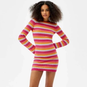 Trendig klänning från Bershka - Superfin stickad klänning från Bershka med färgglada vågiga ränder i rosa, orange, gul, lila och vit. Klänningen är tight, har lång ärm med utsvängda ärmslut, rund halsringning och öppenrygg. Perfekt för dig som gillar färg och mönster!