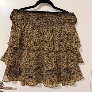 Leopardmönstrad volang kjol  - Säljer en kort kjol med leopardmönster och flera lager volanger. Kjolen har en elastisk midja och är tillverkad i ett lätt, luftigt material som ger en snygg och flowy look.