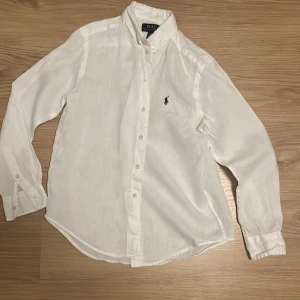 Vit skjorta från Polo Ralph Lauren - Klassisk vit skjorta från Polo Ralph Lauren med lång ärm och knappar framtill. Skjortan har en snygg krage och det ikoniska blå Polo-logot broderat på bröstet. Tillverkad i lätt och skön bomull, perfekt för en clean och stilren look. Storlek M 10-12 år. Jag har använt den vid fåtal tillfällen så det är väldigt bra skick. Jag säljer den för att den är för liten. Jag köpte den för 1095kr och säljer den nu för 449kr. Pris kan diskuteras. För fler frågor kontakta mig privat😊