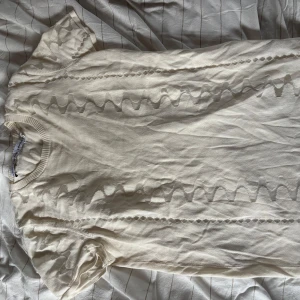 Vit stickad tröja från & Other Stories - Säljer en vit stickad tröja från & Other Stories i storlek S. Tröjan har korta ärmar och ett snyggt, diskret mönster med vågiga detaljer framtill.