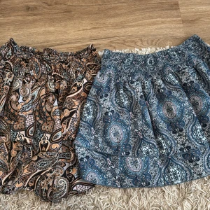 Två paisleymönstrade kjolar från SHEIN - Säljer två korta kjolar från SHEIN med paisleyinspirerat mönster. Ena kjolen har blå och grå toner, den andra har beige, brun och svart. Båda har smockad midja och är gjorda i lätt polyester. Perfekt för dig som gillar boho-vibe och färgglada prints.