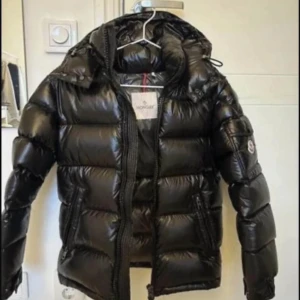 Moncler maya - 🎨 Färg: Svart (Glossy Finish) (Se 2:a bilden för bästa färgåtergivning)  📏 Storlek: 1 (Small / EU 46) Passar herr Small – vänligen kontrollera måtten om osäker.  📐 Mått: (Mått kan ges vid förfrågan)  ♻️ Skick: Ny utan prislapp. Kvitto finns, köpt från Moncler online december 2023. Helt felfri.  🧵 Material: 100% nylon (yttermaterial) med dunfyllning för maximal värme och lätt vikt.  📦 Skickas samma dag vid köp