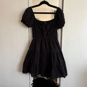 Svart kort klänning - Supersöt svart klänning från SHEIN i strl S med puffärmar och volanger. Modellen har en rundad urringning med knytning framtill!💞