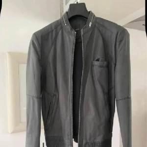 Grå skinnjacka från Emilio, S - Snygg grå skinnjacka från Emilio i storlek S. Jackan har en stilren design med ståkrage, dragkedja framtill och praktiska fickor. Materialet är mjukt skinn och insidan har meshfoder för extra komfort. Perfekt för dig som gillar en clean och modern look.