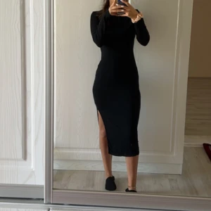 Svart långklänning med slits - Säljerw en svart långklänning med lång ärm och snygg slits på sidan. Klänningen har en tight passform som framhäver figuren och är perfekt för dig som gillar stilrena och minimalistiska looks. Enkel att matcha med smycken och klackar för en cool vibe.