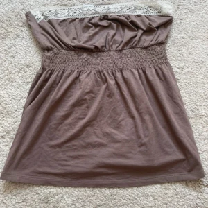 Brun bandeau tubtopp från Intimissimi - Säljer en brun bandeau tubtopp från Intimissimi med bred smock i midjan och snygg spetsdetalj upptill i vitt. Toppen är ärmlös och har en loose passform, perfekt för varma dagar. Materialet är mjuk bomull som känns skönt mot huden. Priset går att diskutera vid snabbt köp!💕