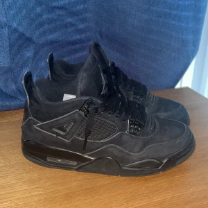 Svarta Nike Jordan 4 sneakers - Säljer ett par svarta Nike Jordan 4 sneakers med snygga meshpaneler och detaljer i mocka. Skorna har klassisk snörning, platt sula och ikonisk Jumpman-logga på plösen. Perfekt för dig som gillar streetwear och vill ha en stilren look.