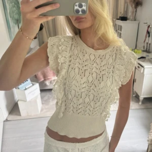 Vit spetsig blus med volang - Superfin vit blus med spetsmönster och breda volangärmar. Toppen har ribbad midja och är ärmlös med rund hals. Perfekt för dig som gillar romantiska detaljer och vill ha en söt, feminin look.