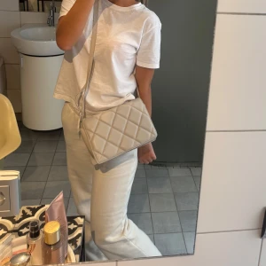 Beige  axelväska - Säljer en stilren beige axelväska  med lång rem. Väskan har en mjuk, vadderad känsla och är perfekt för att bära det viktigaste. Enkel och snygg design som passar till många outfits. 