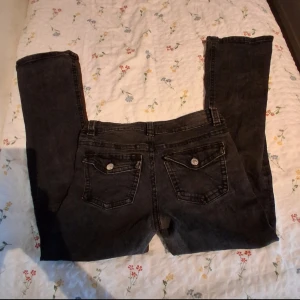 Svarta jeansbyxor från gina - Säljer ett par svarta jeans från gina med klassisk femficksdesign och bootcut ben. Jeansen har silverfärgade knappar och detaljer, samt en mörk tvätt som ger en cool vibe. Perfekt för dig som gillar en y2k och sthlms-stil look.