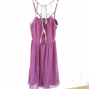 Lila klänning med silvriga detaljer - Lila klänning från Topshop med unika silvriga band och öppna partier vid ryggen. Klänningen har en flowy kjol och coola axelband som ger en edgy vibe. Dragkedja i ryggen för enkel påklädning. Klippt underdelen ca 10cm, man kan få med tyget vid önskemål.