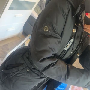 Svart dunjacka med päls från Hollies - Säljer en svart dunjacka från Hollies med  Jackan har flera fickor med dragkedja och knappar, samt en figurnära passform. Använd 2 vintrar! Storlek 36🤍