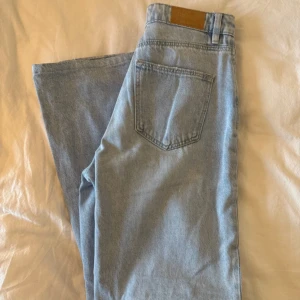 Ljusblå ripped jeans  - Säljer ett par ljusblå jeans med breda raka ben och snygga slitningar vid knäna. Modellen är högmidjad och har klassiska fem fickor och läderpatch bak. Perfekt för dig som gillar en chill och trendig streetstil.