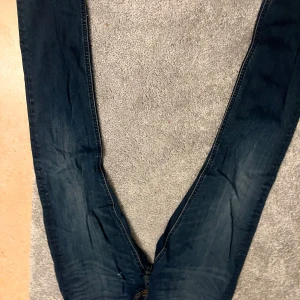 Mörkblå jeans från Lee - Säljer ett par mörkblå jeans från Lee med klassisk femficksdesign och kontrastsömmar i orange. Jeansen har rak passform och är tillverkade i slitstarkt denimtyg. Perfekt för dig som gillar en tidlös och enkel stil.