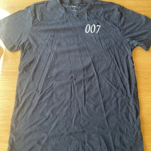 007 Black T-shirt - det är en väldigt fin svart t-shirt med bra design. 007 på bröstet och N.F på nedre delen av ryggen Det finns storlekar S,M och L.