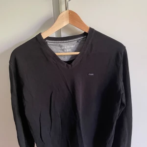 Svart v-ringad tröja Marc O'Polo - Svart långärmad tröja från Marc O'Polo med v-ringad hals och diskret logga på bröstet. Tröjan är i mjuk bomull och har en snygg design. Perfekt för dig som gillar enkel och clean stil. Topp kvalité med inga skador eller liknande.