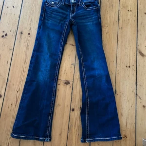 Blå bootcut jeans med kontrastsömmar - Snygga blå jeans med bootcut passform och tydliga vita kontrastsömmar. Klassisk femficksdesign med lock på bakfickorna och silverfärgade knappar. Jeansen har låg midja och är gjorda i jeansmaterial som ger en cool och avslappnad vibe.