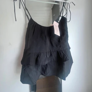 Svart volang linnetopp från Nelly - Svart linnetopp från Nelly med tunna axelband som knyts och dubbla volanger framtill. Toppen har en luftig och flowy passform, perfekt för varma dagar. Materialet är lätt och känns skönt mot huden. Snygg att styla med jeans eller kjol. Helt ny men var tyvärr förstor 💞💞