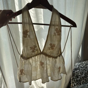 Beige broderad linnetopp Pull&Bear - Supersöt beige linnetopp från Pull&Bear med broderade blommor i ljusrosa. Toppen har djup v-ringning, öppen rygg med knytband med träpärlor i sidorna och volang nedtill. Materialet är lätt och luftigt linne. Så fin topp som tyvärr inte kommer till användning. Endast använd fåtal gånger och storlek S! 🥰