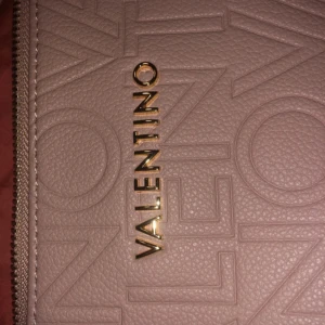 Rosa axelväska från Mario Valentino - Snygg rosa axelväska från Mario Valentino med präglad logga över hela väskan och guldfärgade detaljer. Väskan har justerbar axelrem, dragkedja upptill och en innerficka. Perfekt storlek för dina essentials och kommer med extra rem. Nyköpt och prislappen sitter på, aldrig använd, insåg rakt efter att jag aldrig skulle använda den, inte min stil, nytt pris- 2000, säljer för 1500 men det kan diskuteras 