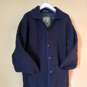 Mörkblå quiltad jacka Oxford Blue - Quiltad jacka från Oxford Blue i mörkblå färg med klassisk krage i manchester. Jackan har tryckknappar framtill och två fickor. Perfekt för dig som gillar stilren och tidlös look. Passar dig som vill ha en jacka med lite extra struktur och detaljer.