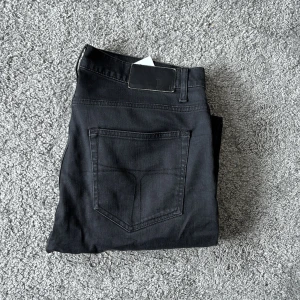 Svarta jeansbyxor Pistolero 34/32 - Svarta jeansbyxor från tiger of Sweden Pistolero i modellen. Klassisk femficksdesign med raka ben och normal passform. Snygga svarta sömmar och diskret läderpatch bak i midjan. Perfekt för dig som gillar stilrena och enkla jeans.