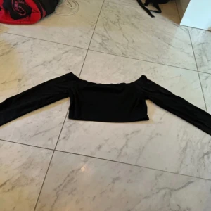 Svart offshoulder croppad topp - Svart croppad topp från Cape Clique med offshoulder-design och långa ärmar. Snygg och enkel stil som passar till många olika outfits. Mjuk och stretchig polyester som sitter skönt och framhäver axlarna.