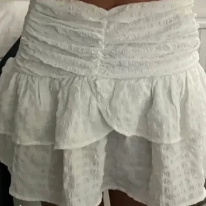 Vit volangkjol med struktur - Supersöt vit kortkjol med volanger och snyggt rynkad midja. Kjolen har en strukturerad yta och dubbla lager som ger extra fluff. Perfekt för dig som gillar romantisk och trendig stil.