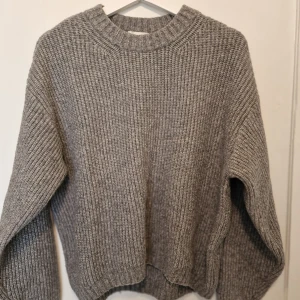 Grå stickad tröja - Grå stickad tröja med grov ribbad struktur och rund hals. Enkel och stilren design som funkar till jeans eller mjukisbyxor.