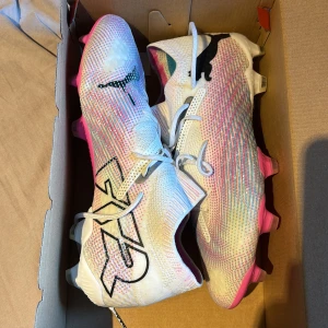 Puma fotbollsskor i vitt och rosa - Säljer ett par grymma Puma fotbollsskor med snyggt mönstrad ovandel i vitt, rosa och silver. Skorna är helt oanvända!