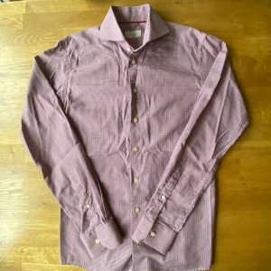 Rutig röd och blå skjorta från Eton - Snygg rutig skjorta från Eton i slim fit, storlek 38. Skjortan har ett klassiskt krage, långa ärmar och knappar framtill. Mönstret är smått rutig i rött, blått och vitt. Perfekt för dig som gillar stilrena och färgglada plagg.