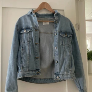 Ljusblå jeansjacka med knappar - Snygg ljusblå jeansjacka från Zara med klassisk krage, två bröstfickor med knapp och silverfärgade detaljer. Jackan har raka långa ärmar och knappar framtill. Perfekt för dig som gillar en chill och tidlös stil.
