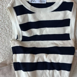 Randig ärmlös topp från Zara - Snygg ärmlös topp från Zara i storlek M med breda svarta och vita ränder. Rund halsringning och mjukt stickat material som känns skönt mot huden. Perfekt för dig som gillar klassisk stil med en modern twist.
