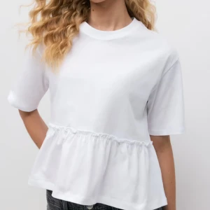 Vit volangtop från Gina Tricot - Supersöt vit topp från Gina Tricot med volangdetalj nedtill som ger en chill och trendig vibe. Rund halsringning och korta ärmar, perfekt till jeans eller kjol. Mjuk bomullskvalitet som känns skön mot huden. Knappt använd