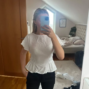 Vit blus med volang och smock - Säljer en söt vit blus med korta ärmar, smockad midja och volang nertill. Aldrig använd🩷