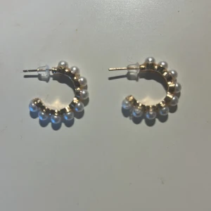 Guldiga hoops med pärlor - Snygga örhängen i form av små hoops i guldton med vita pärlor runt hela ringen. Perfekt accessoar för att lyfta din look med en touch av elegans och trendig vibe. Lätta att bära och passar till många stilar.💞