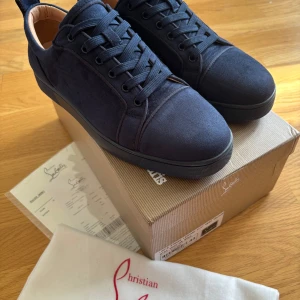 Mörkblå sneakers från Christian Louboutin - Snygga mörkblå sneakers från Christian Louboutin i mocka med klassisk röd sula och rund tå. Skorna har snörning och diskreta ventilationshål på sidan. Perfekta för dig som vill sticka ut med exklusiva detaljer och lyxig känsla.de är använda ett fåtal gånger och skicket är mycket bra,bara några skrapmärken som ni ser på bilderna. Har ni frågor så är det bara att kontakta mig😀